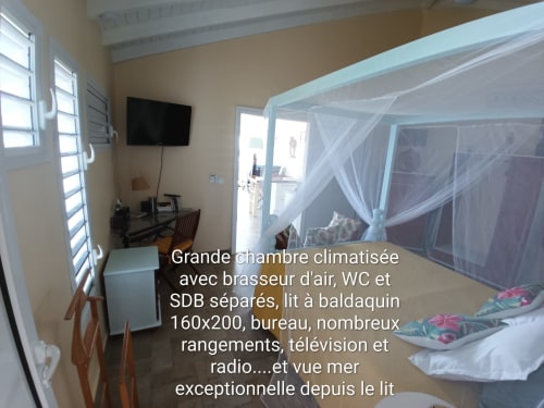 Chambre spacieuse climatisée aux Colibris Amoureux avec lit à baldaquin, bureau, TV et vue sur mer à Grand Bourg