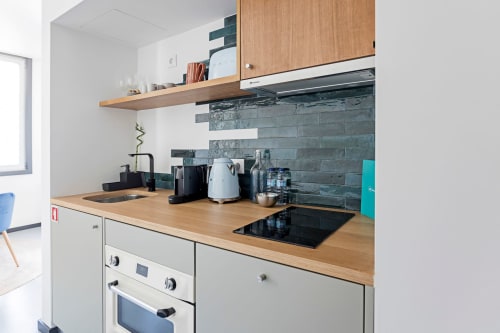 Modern studio apartment kitchenette in Porto with wooden countertop, slate backtile, white cabinetry, induction cooktop, and