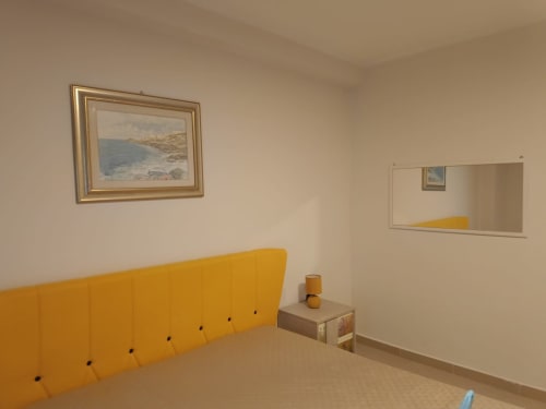 Luminosa camera da letto a Domus Smartrooms a Sellia con testata gialla, opere d'arte costiera e specchio