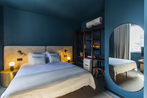 Modern hotel bedroom with blue walls, bed with yellow headboard, round mirror, and air conditioning in Porto