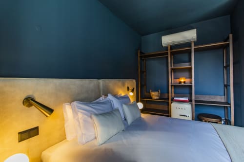 Modern bedroom in Porto hotel with blue walls, gray bed, wooden shelving, warm lighting, and air conditioning unit