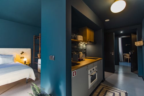 Modern studio apartment in Porto with turquoise walls, bedroom area with white bedding, and open-plan kitchenette with wooden