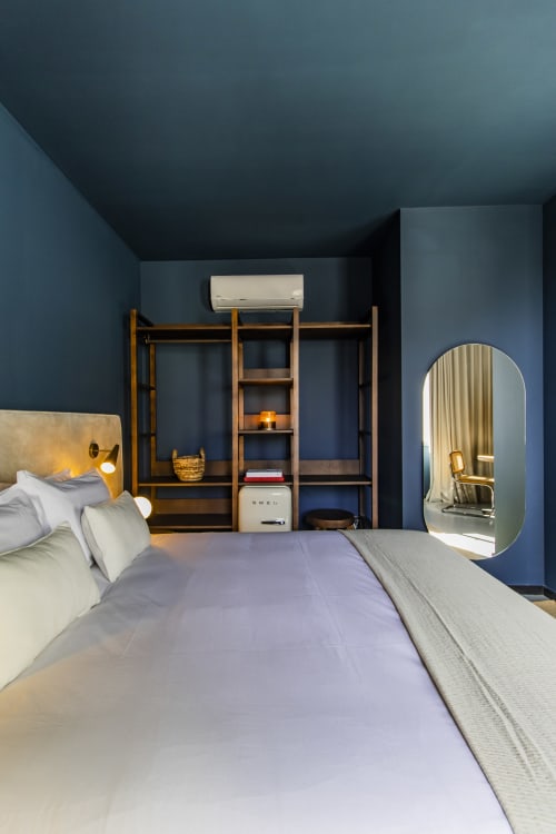 Modern bedroom in Porto hotel with blue walls, wooden shelving, bed with white linens, arched mirror, and air conditioning