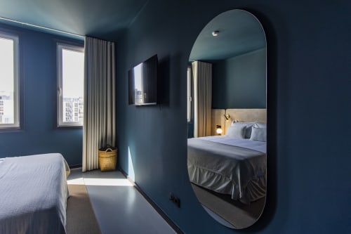 Modern Porto hotel bedroom with deep blue walls, round mirror, bed with white linens, and city views through windows