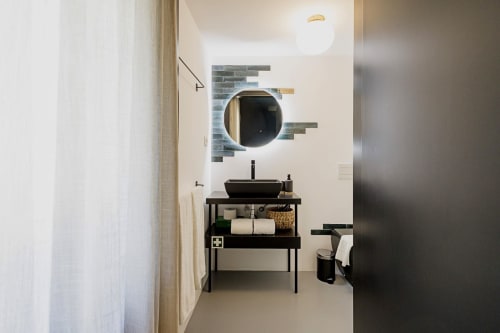 Modern bathroom in Benefit Collection Porto hotel with round mirror, black vessel sink, and minimalist black vanity with