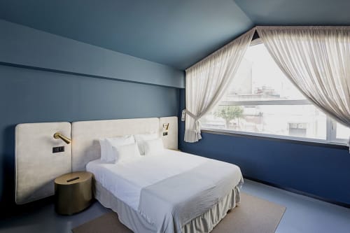 Modern bedroom in Porto hotel duplex with blue walls, white bed, brass fixtures, and city views through sheer curtains
