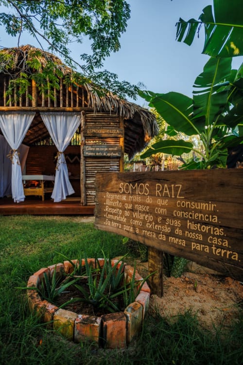 Bangalô rústico com teto de palha e cortinas brancas na La Cozinha Pousada, Cajueiro da Praia, cercado de plantas tropicais