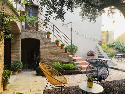 Charmante cour de jardin à La Vieille Demeure à Torreilles avec chaise jaune, escaliers en pierre, plantes en pot et style rustique