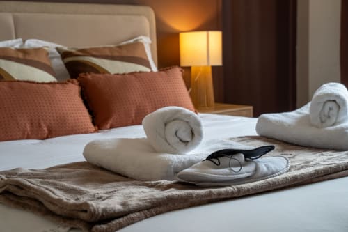 Lit luxueux avec serviettes blanches roulées, pantoufles et équipements de l'hôtel Le 1 Péraudel à Castres