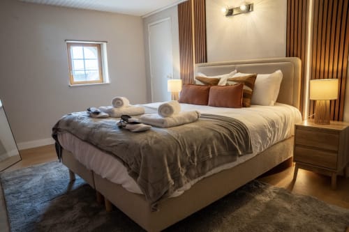 Chambre luxueuse au Le 1 Péraudel à Castres : lit capitonné beige, accents marron, éclairage chaleureux et vue sur la ville