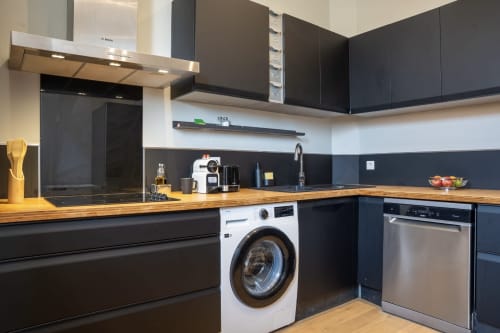 Cuisine moderne noire avec plan de travail en bois, lave-linge blanc et électroménagers en acier inoxydable au Loft Prestige du 1