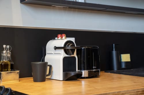 Machine à café Nespresso blanche avec tasse noire et accessoires sur plan de travail en bois dans la cuisine de l'appartement-hôtel de Castres
