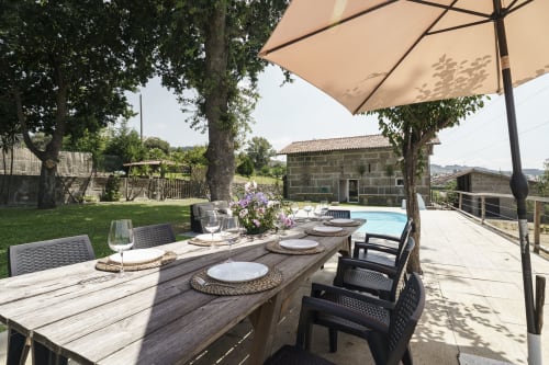 Espaço de refeições no jardim da Quinta de Carvalhal com guarda-sóis, mesa de madeira e vista para a piscina em Guimarães