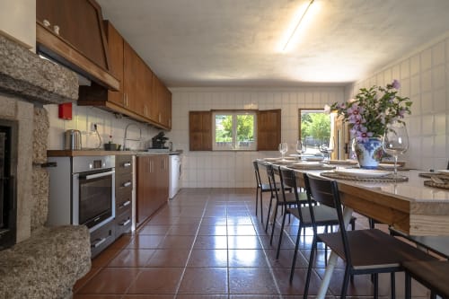 Espaçosa cozinha e zona de refeições na Quinta de Carvalhal Casa da Vinha em Guimarães com marcenaria em madeira, vistas para o jardim, e