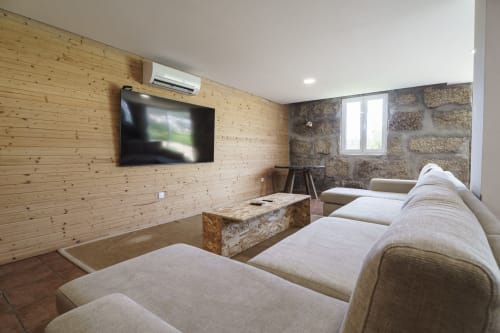 Sala de estar moderna na Quinta de Carvalhal com sofás creme, parede de pedra, painéis de madeira, TV de tela plana e jardim