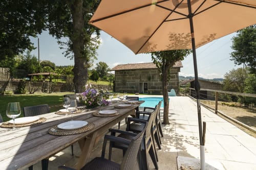 Quinta de Carvalhal com mesa de jantar ao ar livre, guarda-sol bege, piscina privada e casa de pedra em jardim em Guimarães
