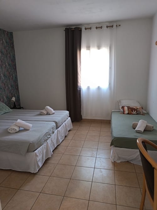 Chambre triple au Clos du Thoronet avec deux lits, draps blancs, carrelage et fenêtre avec rideaux