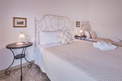 Camera tripla Casa Mia B&B con letto in ferro battuto, biancheria bianca, comodino scuro con lampada e quadri su pareti lavanda
