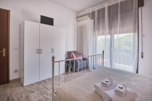 Camera luminosa a Casa Mia B&B con letto matrimoniale, letto singolo, guardaroba bianco, TV a schermo piatto e balcone con vista sul giardino