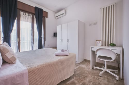 Ampia camera da letto a Casa Mia B&B con letto matrimoniale, armadio bianco, scrivania, porte verso balcone e vista sulla città