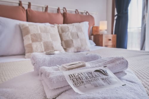 Asciugamani piegati con articoli Beauty Therme sul letto della camera Casa Mia B&B, con testata rosa e vista sulla città