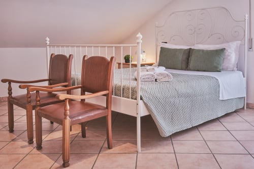 Spaziosa camera familiare a Casa Mia B&B con letto in ferro bianco, cuscini verdi, sedie in legno, mattonelle in terracotta e toni rosa tenui
