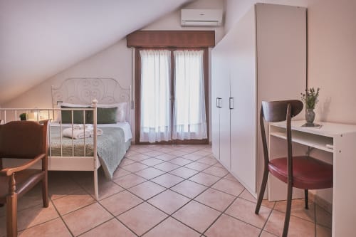 Camera da letto luminosa in mansarda presso Casa Mia B&B in Italia con letto in ferro battuto, armadio bianco, scrivania, pavimento in terracotta e balcone