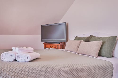 Camera accogliente a Casa Mia B&B con letto, cuscini, asciugamani arrotolati e TV a schermo piatto su baule arancione