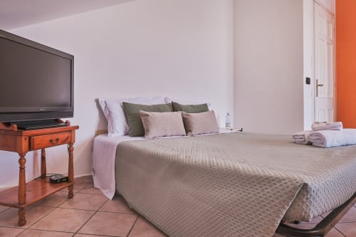 Spaziosa camera da letto a Casa Mia B&B con letto queen, cuscini verdi e rosa, TV a schermo piatto su mobile in legno e accenti arancioni