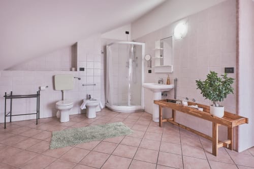 Bagno spazioso di Casa Mia B&B con piastrelle rosa, box doccia, lavabo, WC, bidet e mobile in legno con piante