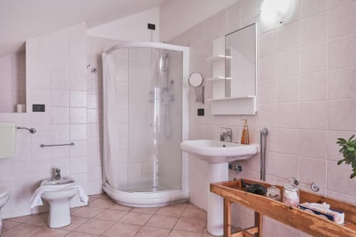 Bagno con piastrelle rosa presso Casa Mia B&B con doccia angolare, lavabo a colonna e vanità in legno nella camera d'albergo italiana
