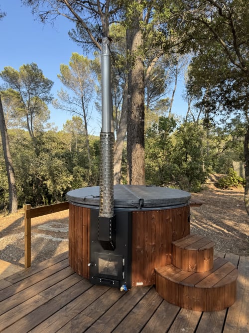 Bain à remous en bois avec cheminée en métal sur une terrasse entourée d'arbres au Domaine d'Olga à Aniane, France