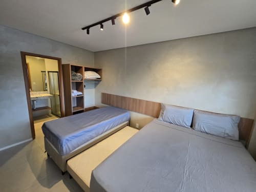 Quarto moderno no Labedi Apartamentos com duas camas, cabeceiras de madeira, banheiro privativo e iluminação em trilho em Maceió