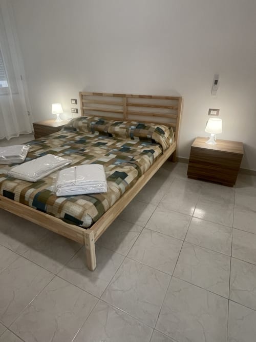 Ampia camera da letto in appartamento a Termoli con letto in legno, biancheria a fantasia, comodini con lampade e pavimento in piastrelle
