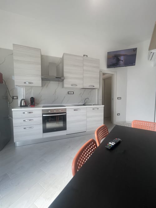 Cucina e zona pranzo moderna dell'appartamento Nautilus a Termoli, con mobili bianchi, forno integrato e sedie arancioni