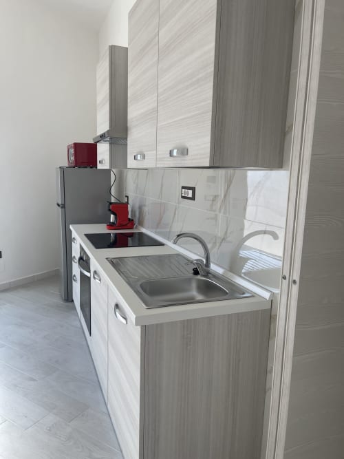 Cucinetta moderna con lavello in acciaio inossidabile, mobili bianchi e macchina da caffè rossa nell'appartamento Casa Vacanze Nautilus,