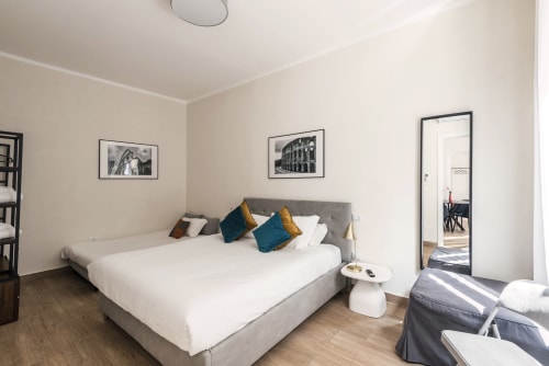 Camera moderna a Flavia's Holiday Home di Roma con letto imbottito grigio, cuscini turchesi e quadri con cornice nera