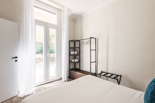 Luminosa camera da letto nella casa vacanze di Flavia a Roma con pareti bianche, porte in vetro verso la terrazza e moderni scaffali in metallo nero