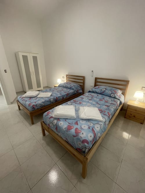 Camera da letto luminosa con tre letti in legno, biancheria blu a motivi e lenzuola bianche presso Rigiariloo Home Apartments
