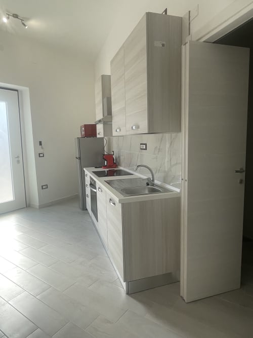 Cucina moderna nell'appartamento di Termoli con lavello in acciaio inox, mobili bianchi e pavimento piastrellato grigio
