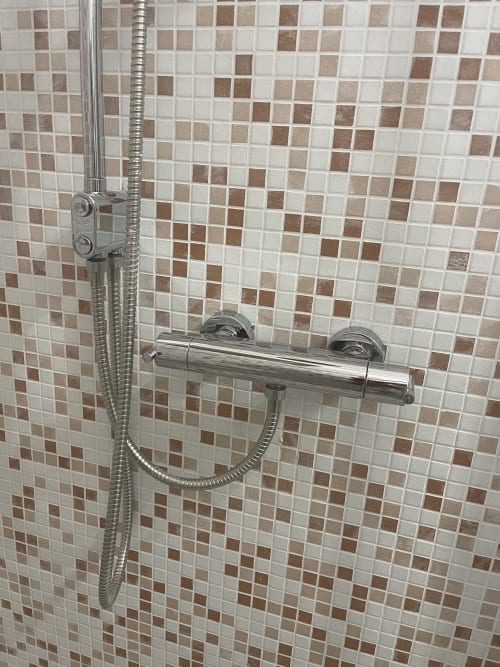 Soffione doccia e rubinetteria cromata su parete rivestita in piastrelle beige e marrone nel bagno di Rigiariloo Home Apartments