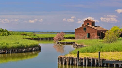 Rustica casa colonica in mattoni rossi circondata da verdi campi e canali d'acqua a Porto Viro, Italia