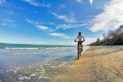 Ciclista in spiaggia sabbiosa vicino a Porto Viro con mare turchese e cielo azzurro
