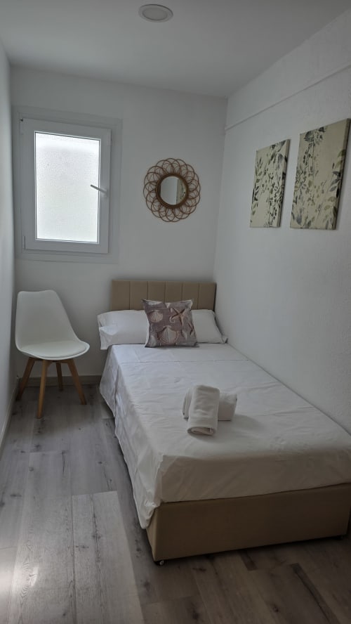 Acogedor estudio en casita de Benicàssim con cama individual, silla blanca, espejo de mimbre y vistas al jardín