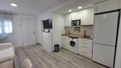 Cocineta moderna con gabinetes blancos, lavadora y TV de pantalla plana en cabaña frente al mar en Oropesa