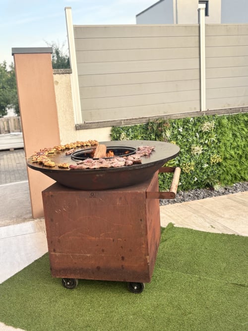 Outdoor fire pit grill at Hôtel-Restaurant le S'Y in Seingbouse with meat cooking and modern fence backdrop