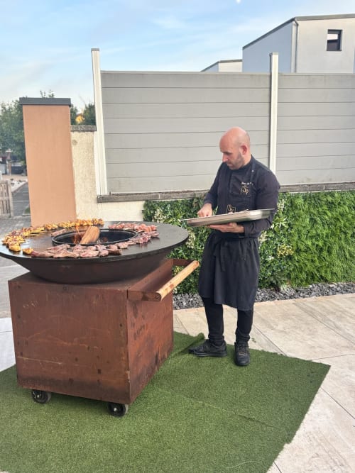 Chef preparing food at outdoor fire pit grill at Hôtel-Restaurant le S'Y in Seingbouse