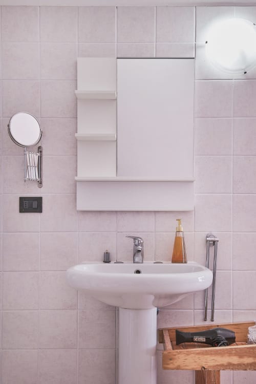 Bagno moderno di Casa Mia B&B a Porto Viro con piastrelle rosa, lavandino bianco e scaffali a muro