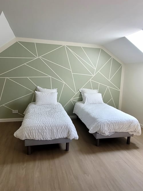 Deux lits jumeaux aux draps blancs dans une chambre moderne avec un mur d'accent géométrique vert au Clos de la