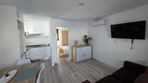Interior moderno de apartamento en Monica Socarici, Benicàssim con cocina americana, sala de estar, sofá, TV y acceso a dormitorio